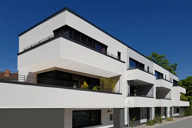 Perspektivische Außenaufnahme einer modernen Wohnanlage mit gestaffelten Balkonen und Flachdach unter strahlend blauem Himmel.