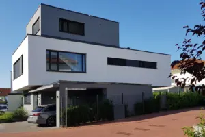 Seitenansicht eines modernen Mehrfamilienhauses am Bertha-von-Suttner-Weg mit weißer Putzfassade und grauen Akzentbereichen.