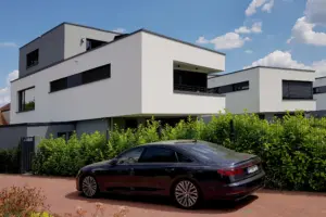 Perspektivische Aufnahme einer modernen Wohnanlage mit weißen Fassaden, dunklen Fensterrahmen und einer schwarzen Limousine im Vordergrund.