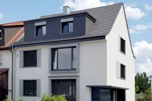 Straßenansicht eines modernen Hauses mit weißer Fassade, grauen Fensterumrandungen und einem anthrazitfarbenen Satteldach mit Gauben.