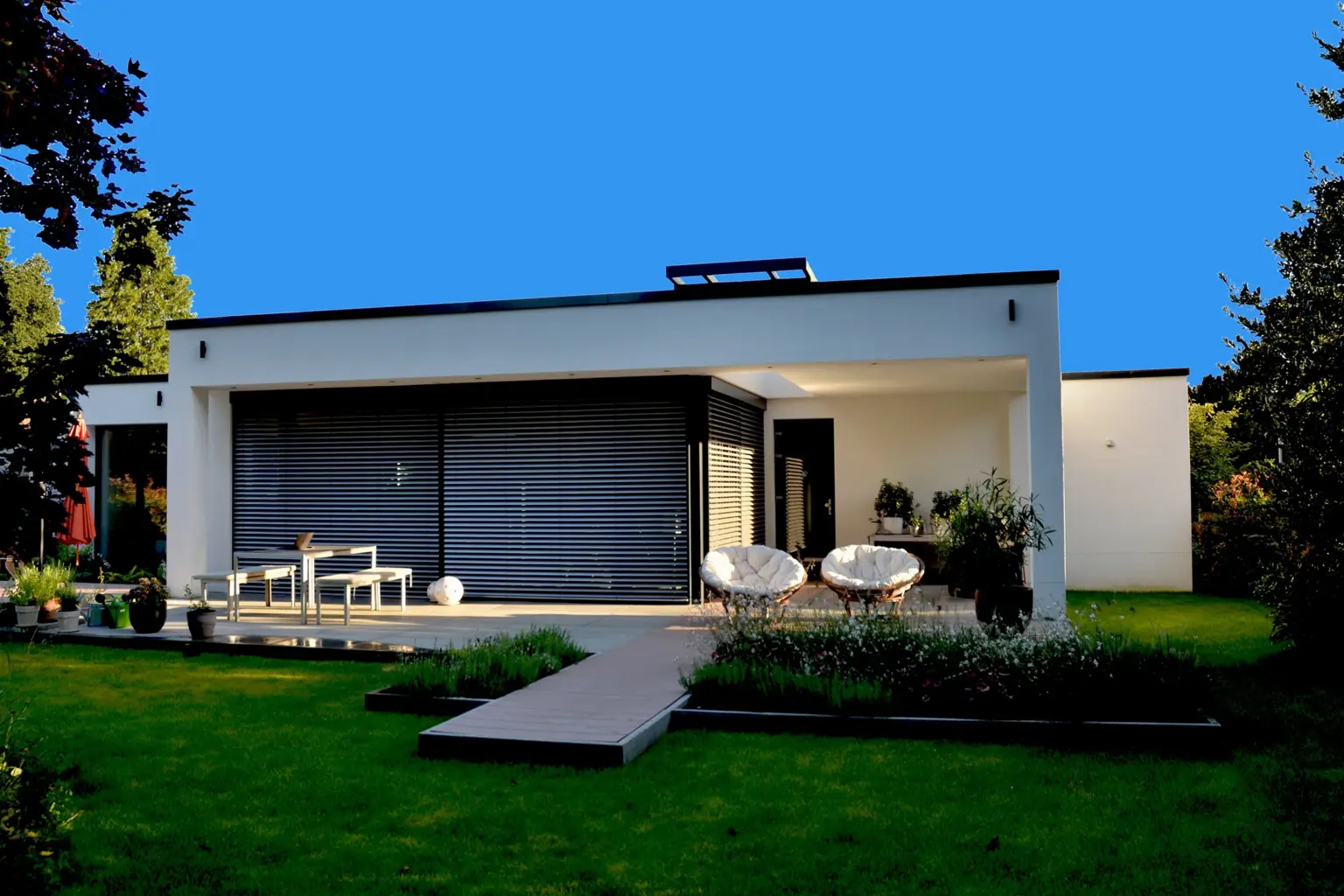 Außenansicht des beleuchteten Wohnhauses mit geschlossenen Raffstores, einer gepflegten Rasenfläche und moderner Gartenbeleuchtung.