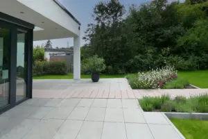 Detail der Terrassengestaltung: Großformatige graue Steinplatten kombiniert mit einem Holzsteg, der durch moderne Beetbepflanzung führt.