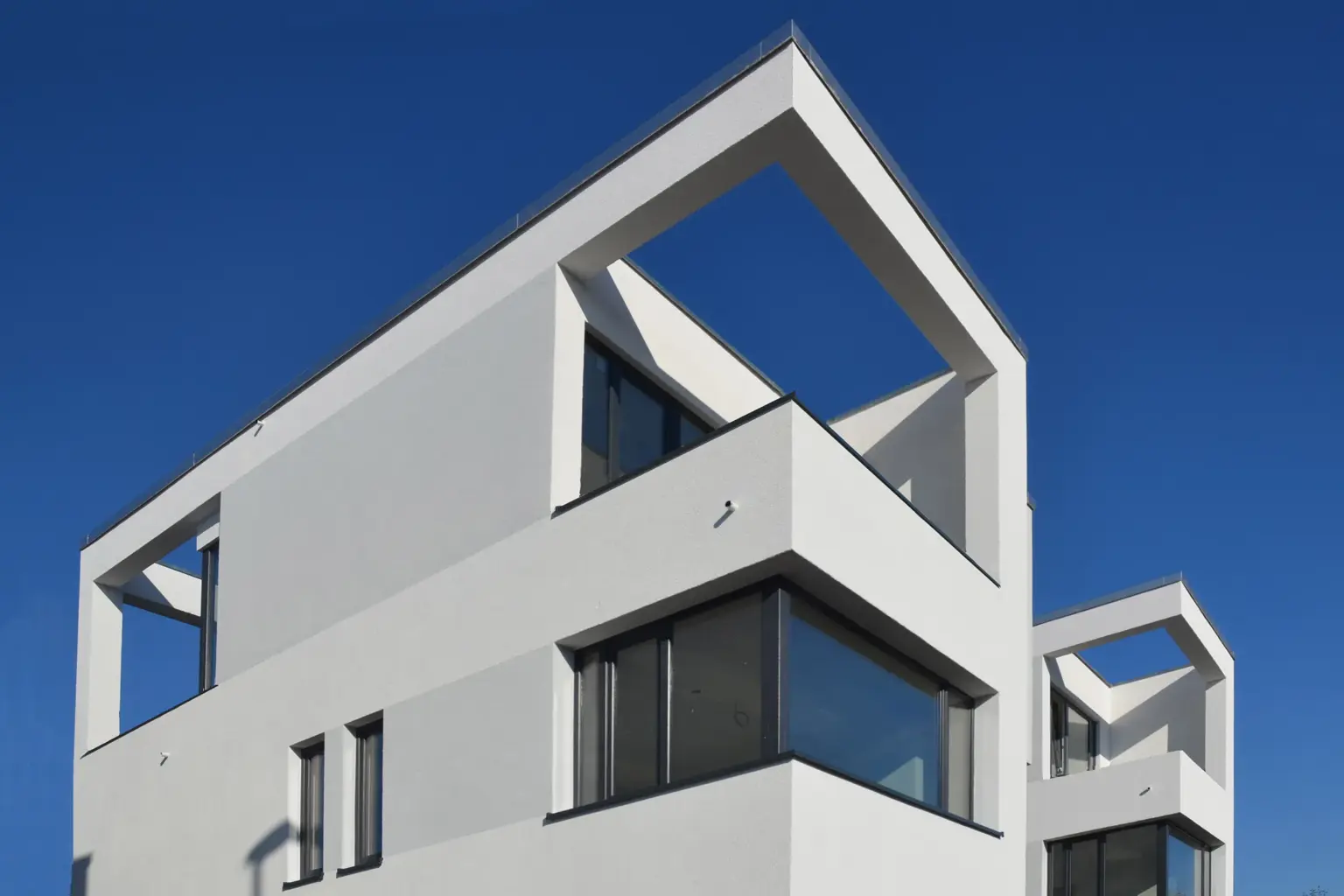 Froschperspektive eines modernen Gebäudes mit markanten, rechteckigen Dachausschnitten vor strahlend blauem Himmel.