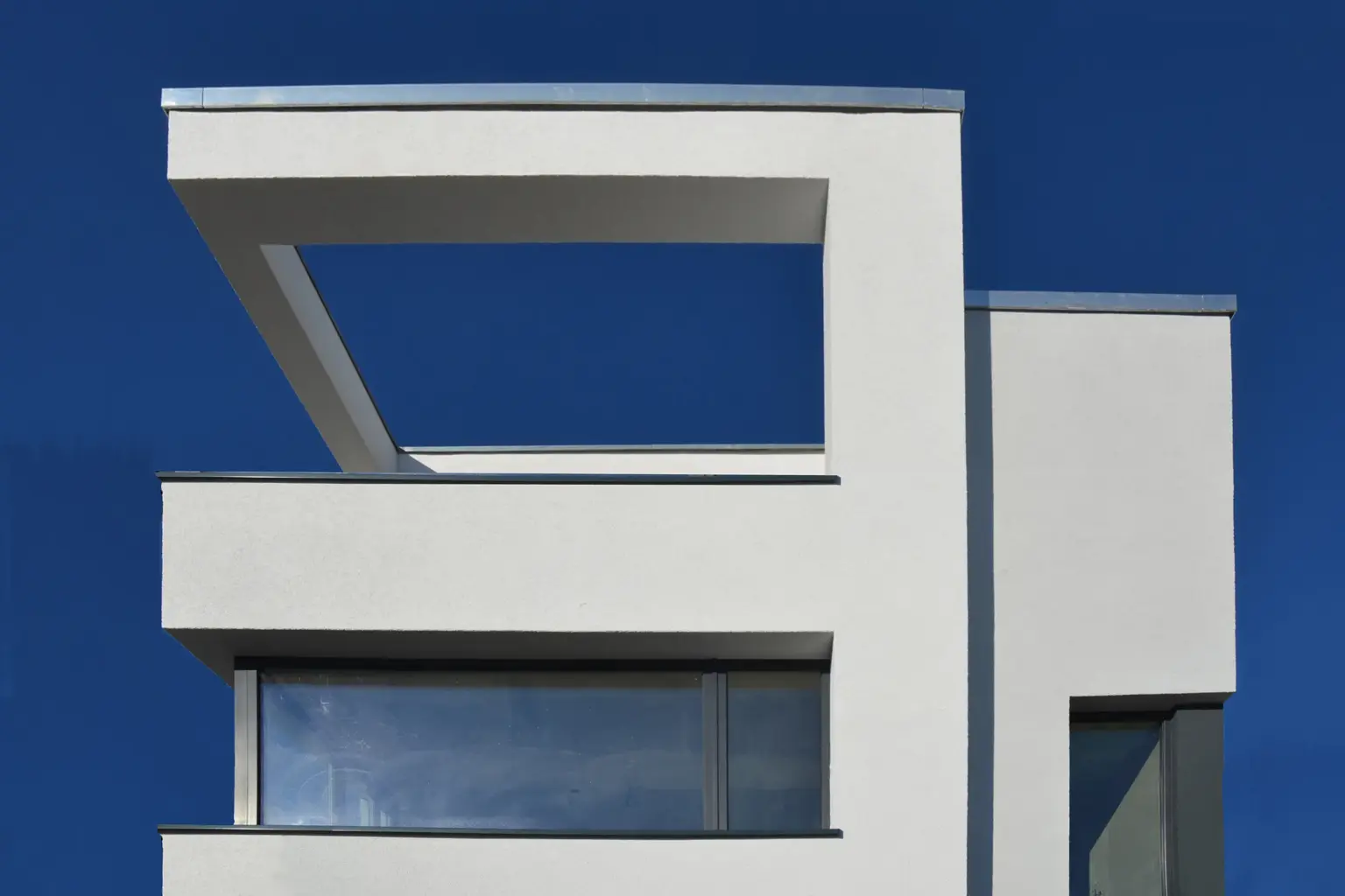 Architektur-Detail: Ein offener, rahmenartiger Dachaufbau an einem modernen kubischen Haus gegen einen tiefblauen Himmel.