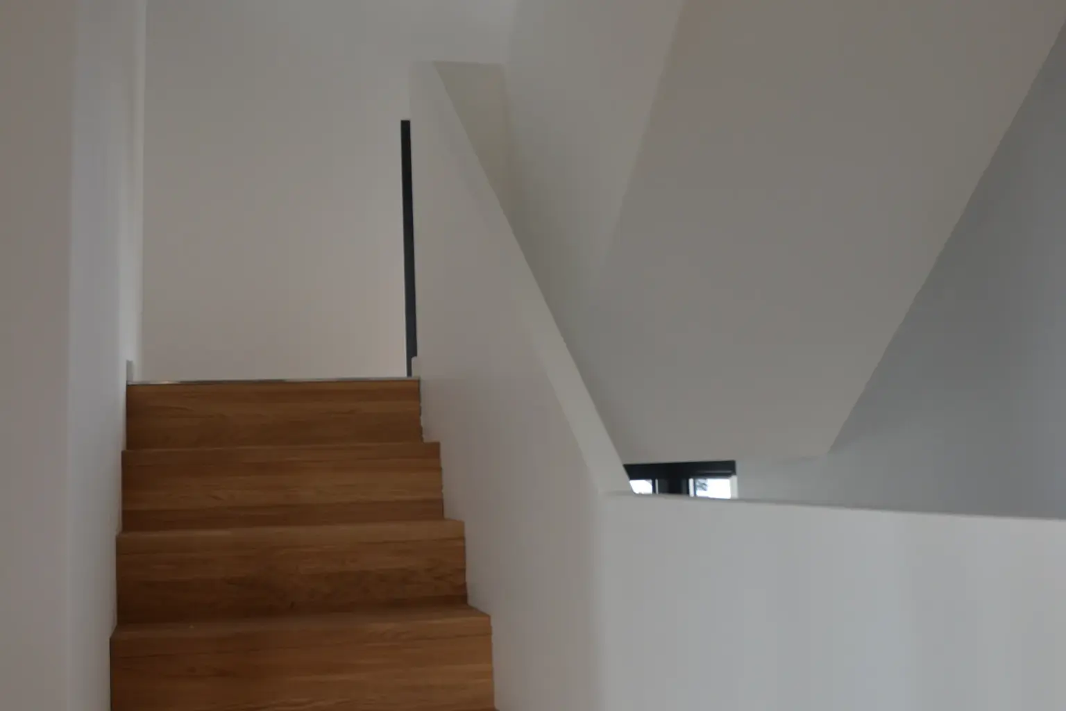 Minimalistisches Treppenhaus in einem modernen Wohnhaus mit einer Holztreppe und schlichten weißen Wandflächen.