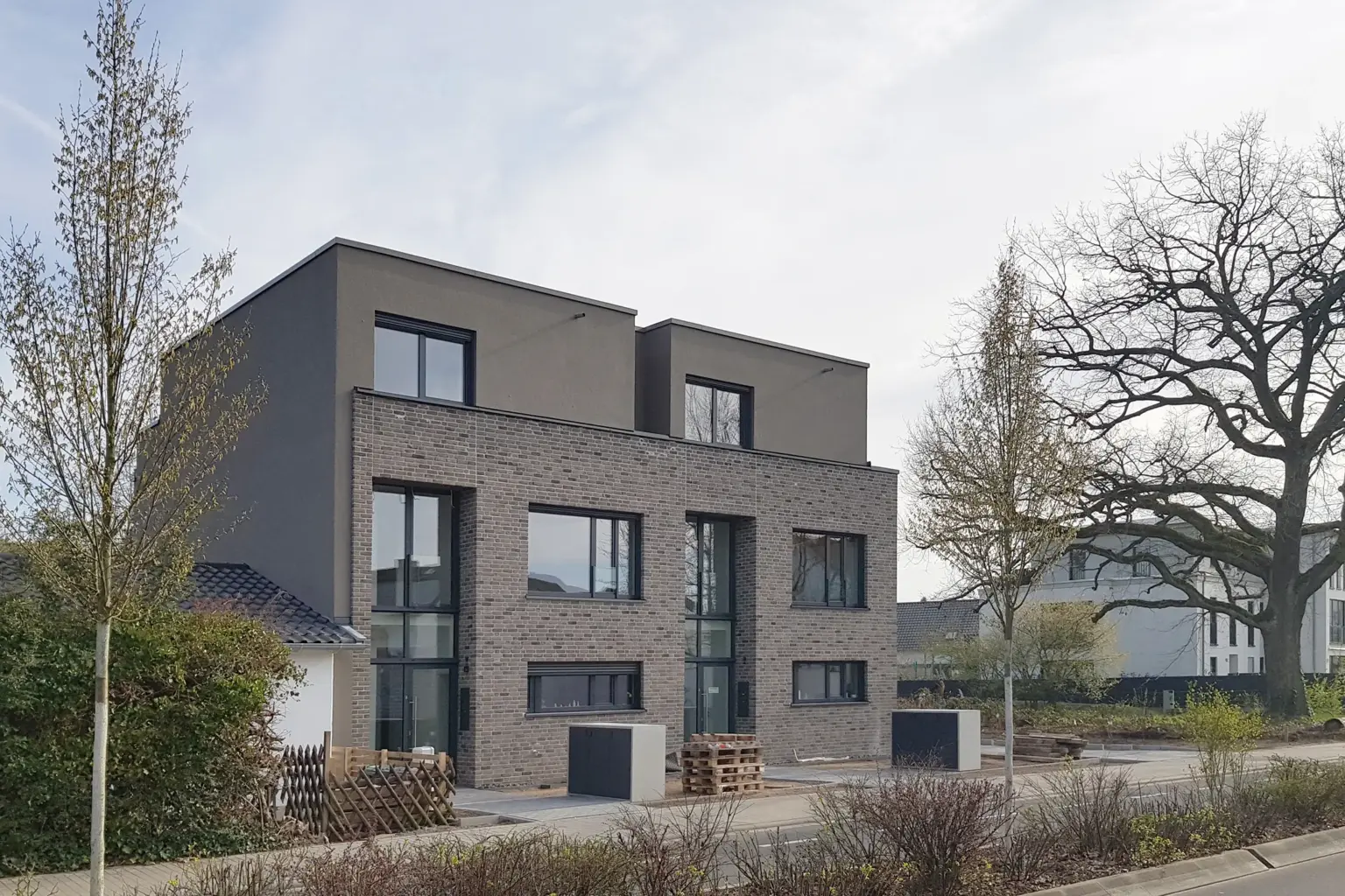 Frontale Ansicht eines Mehrfamilienhauses in Klinkerbauweise mit großen Fensterfronten und minimalistisch gestalteten Eingangsbereichen.