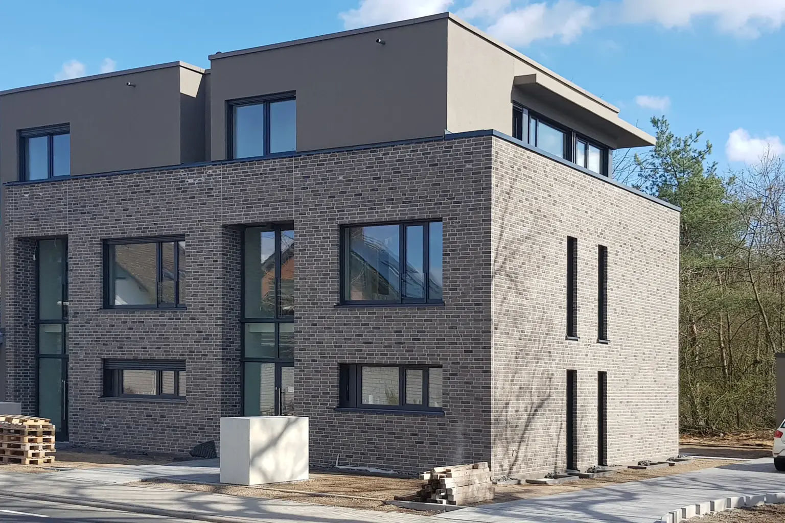 Perspektivische Aufnahme der Gebäudeecke, die das Zusammenspiel von grauem Backstein und glattem, beigem Putz im Obergeschoss zeigt.