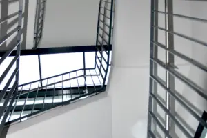 Froschperspektive in einem modernen Treppenhaus; die geometrischen Linien der schwarzen Metallgeländer bilden einen starken Kontrast zu den weißen Wänden.