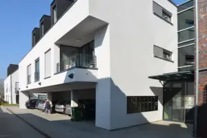 Außenansicht einer modernen Wohnanlage mit Carport im Erdgeschoss, weißen Balkonbrüstungen und einem verglasten Eingangsbereich.