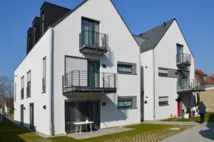 Rückansicht zweier moderner Wohnhäuser mit Satteldach, weißen Fassaden und übereinanderliegenden Balkonen mit schwarzen Metallgittern.