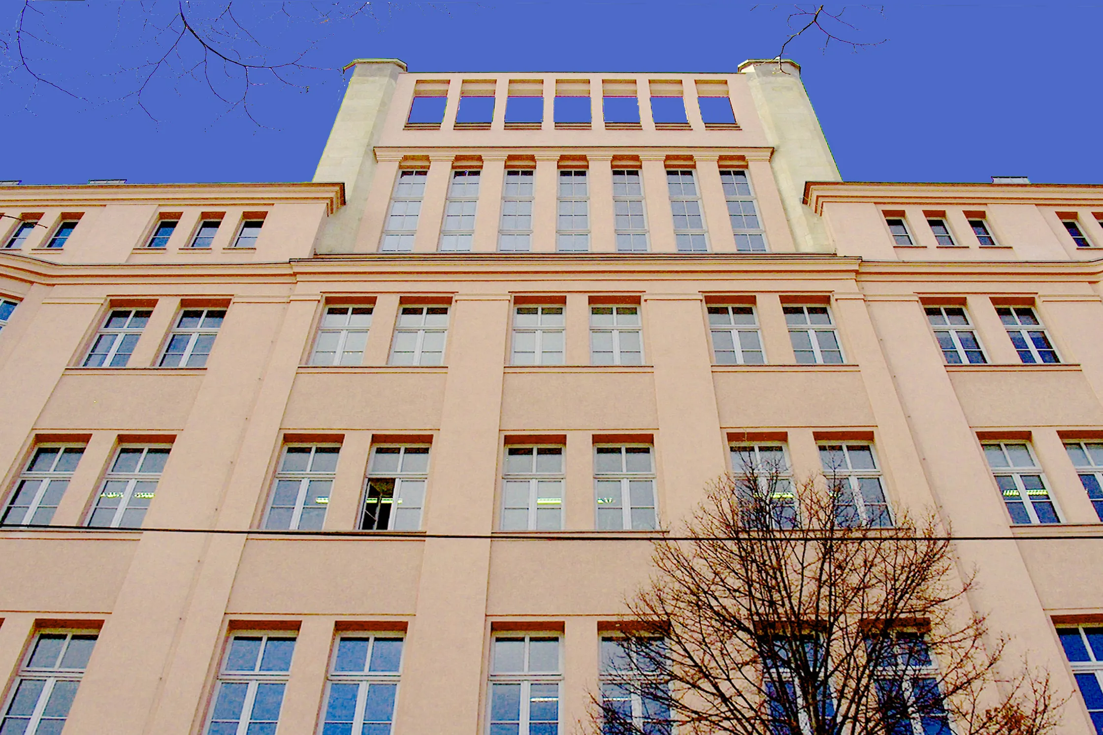 Monumentale Fassadenansicht eines historischen, mehrstöckigen Gebäudes mit regelmäßigem Fensterraster unter strahlend blauem Himmel.
